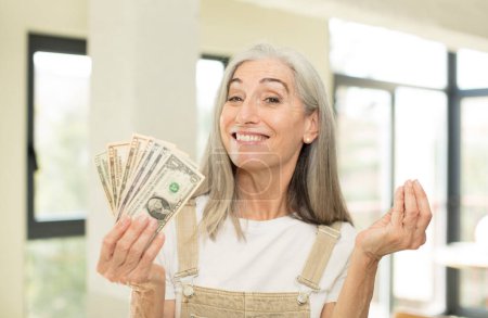 Photo for Pretty senior woman smiling cheerfully, feeling happy and pointing to the side. with dollar banknotes - Royalty Free Image
