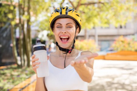 Photo for Young pretty woman smiling happily and offering or showing a concept. bike helmet concept - Royalty Free Image