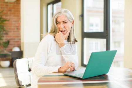 Photo for Senior pretty woman with mouth and eyes wide open and hand on chin with a laptop - Royalty Free Image