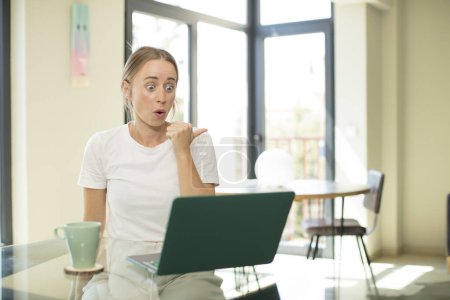 Photo for Caucasian pretty woman with a laptop looking astonished in disbelief, pointing at object on the side and saying wow, unbelievable - Royalty Free Image