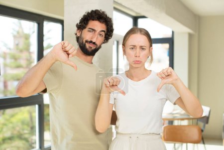 Photo for Young adult couple looking sad, disappointed or angry, showing thumbs down in disagreement, feeling frustrated - Royalty Free Image