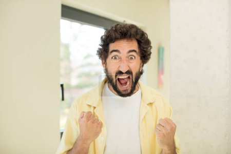Photo for Young crazy bearded man shouting aggressively with annoyed, frustrated, angry look and tight fists, feeling furious - Royalty Free Image