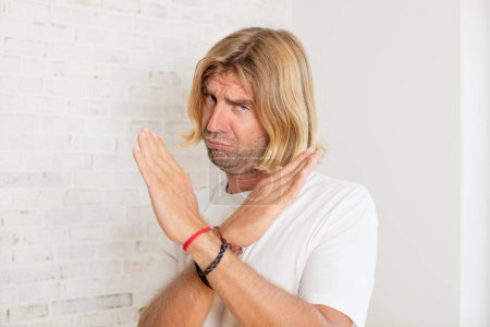 Photo for Young blond adult man looking annoyed and sick of your attitude, saying enough! hands crossed up front, telling you to stop - Royalty Free Image
