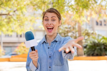Photo for Young pretty woman smiling happily and offering or showing a concept. presenter and microphone concept - Royalty Free Image