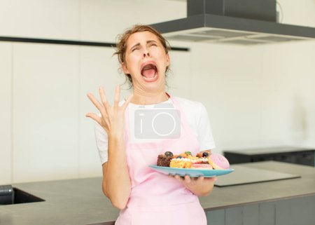 Photo for Young pretty woman screaming with hands up in the air. home made cakes concept - Royalty Free Image