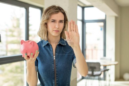 Photo for Pretty woman looking serious showing open palm making stop gesture. piggy bank concept - Royalty Free Image