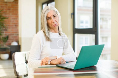 Foto de Anciana bonita mujer sintiéndose triste y quejumbroso con una mirada infeliz y llorando con un ordenador portátil - Imagen libre de derechos