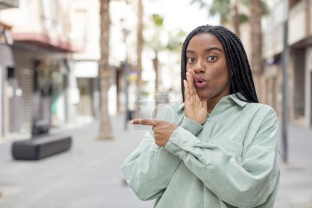 Téléchargez les photos : Afro jolie femme noire se sentant surprise avec une expression choquée et pointant vers le côté - en image libre de droit