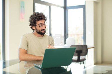 Photo for Young adult bearded man with a laptop pointing at camera with a satisfied, confident, friendly smile, choosing you - Royalty Free Image