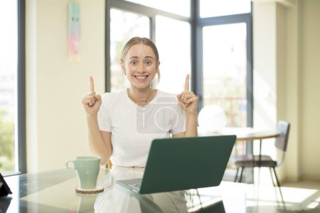Foto de Mujer guapa caucásica con un ordenador portátil sensación de asombro y boca abierta apuntando hacia arriba con una mirada sorprendida y sorprendida - Imagen libre de derechos