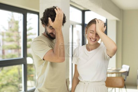 Photo for Young adult couple laughing and slapping forehead like saying doh! I forgot or that was a stupid mistake - Royalty Free Image