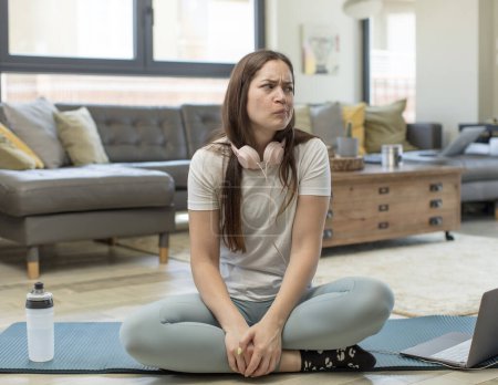 Foto de Mujer adulta joven practicando yoga preguntándose, pensando pensamientos e ideas felices, soñando despierto, buscando copiar espacio al lado - Imagen libre de derechos