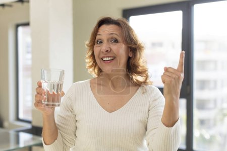 Foto de Mujer bonita de mediana edad sintiéndose como un genio feliz y emocionado después de darse cuenta de una idea. vaso de agua - Imagen libre de derechos