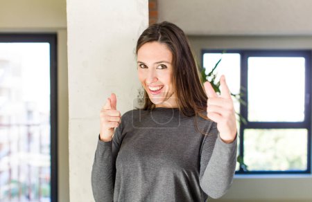 Photo for Young adult pretty woman smiling with a positive, successful, happy attitude pointing to the camera, making gun sign with hands - Royalty Free Image