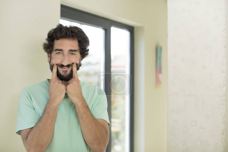 Photo for Young crazy bearded man smiling confidently pointing to own fake smile - Royalty Free Image