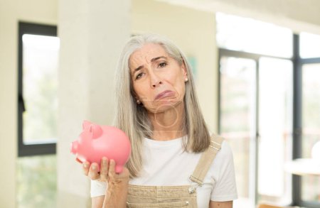 Photo for Pretty senior woman feeling sad and whiney with an unhappy look and crying. with a piggy bank - Royalty Free Image