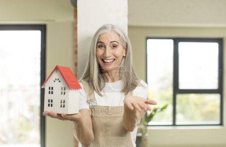 Photo for Pretty senior woman smiling happily and offering or showing a concept. with a house model - Royalty Free Image