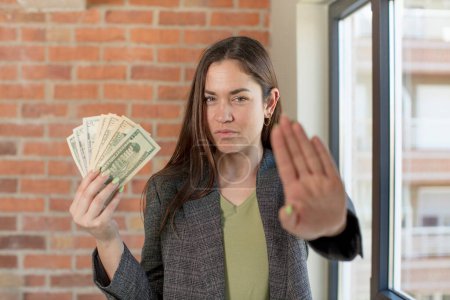 Photo for Young pretty woman looking serious showing open palm making stop gesture. dollar banknotes concept - Royalty Free Image