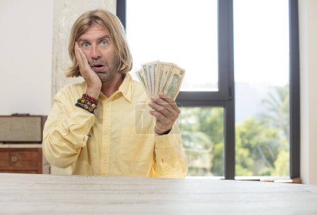 Foto de Joven hombre caucásico adulto sintiéndose extremadamente sorprendido y sorprendido. concepto de billetes en dólares - Imagen libre de derechos
