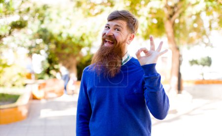 Photo for Red hair bearded man feeling happy, relaxed and satisfied, showing approval with okay gesture, smiling - Royalty Free Image