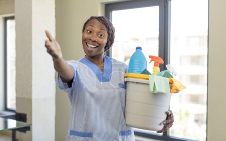 Foto de Negro afro mujer sonriendo felizmente y ofreciendo o mostrando un concepto con productos limpios. concepto de ama de llaves - Imagen libre de derechos