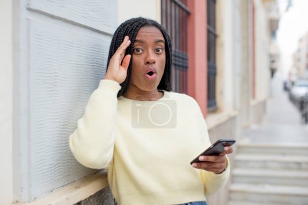 Téléchargez les photos : Noir afro femme regardant heureux, étonné et surpris. utilisant un concept de smartphone - en image libre de droit