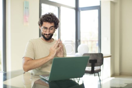 Photo for Young adult bearded man with a laptop feeling proud, mischievous and arrogant while scheming an evil plan or thinking of a trick - Royalty Free Image