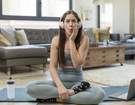Photo for Young adult woman practicing yoga feeling shocked and astonished holding face to hand in disbelief with mouth wide open - Royalty Free Image
