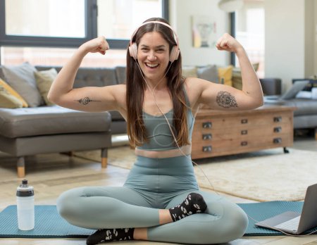 Foto de Joven mujer adulta practicando yoga sintiéndose feliz, satisfecha y potente, flexing fit y bíceps musculares, luciendo fuerte después del gimnasio - Imagen libre de derechos