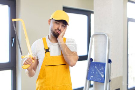Photo for Young handsome man feeling bored, frustrated and sleepy after a tiresome. handyman with a saw - Royalty Free Image