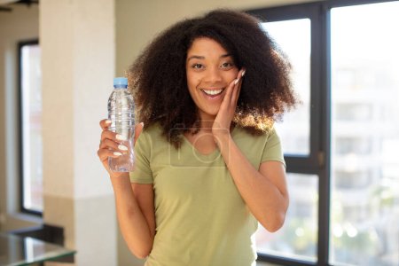 Téléchargez les photos : Jolie afro femme noire se sentant heureuse et étonnée de quelque chose d'incroyable. concept de bouteille d'eau - en image libre de droit