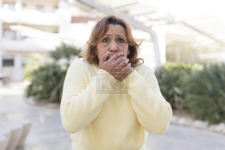 Foto de Mujer de mediana edad que cubre la boca con las manos con una expresión sorprendida, sorprendida, manteniendo un secreto o diciendo oops - Imagen libre de derechos