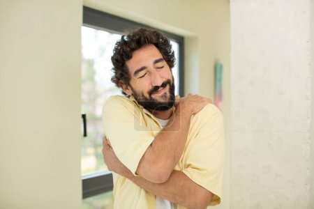 Photo for Young crazy bearded man feeling in love, smiling, cuddling and hugging self, staying single, being selfish and egocentric - Royalty Free Image