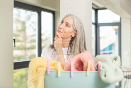 Photo for Pretty senior woman smiling with a happy, confident expression with hand on chin. washing clothes concept - Royalty Free Image