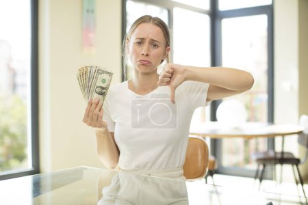 Photo for Young pretty caucasian woman feeling cross,showing thumbs down. dollar banknotes concept - Royalty Free Image