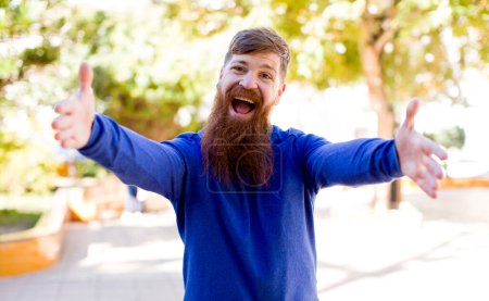 Photo for Red hair bearded man smiling cheerfully giving a warm, friendly, loving welcome hug, feeling happy and adorable - Royalty Free Image