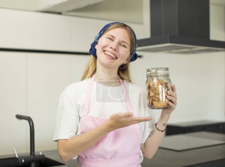 Téléchargez les photos : Jeune jolie femme souriant joyeusement, se sentant heureuse et montrant un concept. biscuits faits maison - en image libre de droit