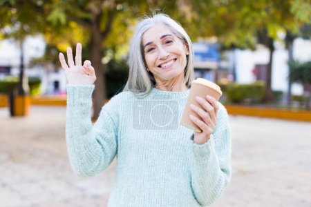 Foto de Mujer bastante mayor sintiéndose feliz, mostrando aprobación con gesto bien con un café para llevar - Imagen libre de derechos