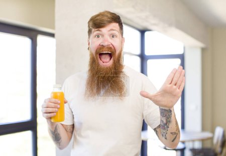 Photo for Red hair man feeling happy and astonished at something unbelievable with an orange juice bottle - Royalty Free Image