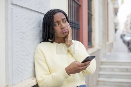 Téléchargez les photos : Noir afro femme se sentir ennuyé, frustré et somnolent après un fatigant. utilisant un concept de smartphone - en image libre de droit