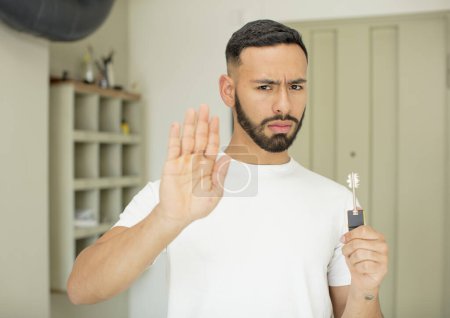 Foto de Joven hombre adulto mirando serio mostrando la palma abierta haciendo gesto de parada. concepto clave para el hogar - Imagen libre de derechos