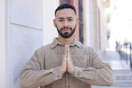 Photo for Young handsome man feeling worried, hopeful and religious, praying faithfully with palms pressed, begging forgiveness - Royalty Free Image