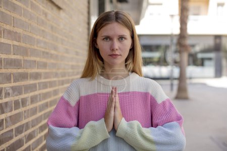 Foto de Bonita joven sintiéndose preocupada, esperanzada y religiosa, orando fielmente con las palmas presionadas, rogando perdón - Imagen libre de derechos