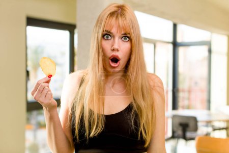 Téléchargez les photos : Jeune jolie femme tenant une frite pomme de terre malsaine à l'intérieur de la maison - en image libre de droit