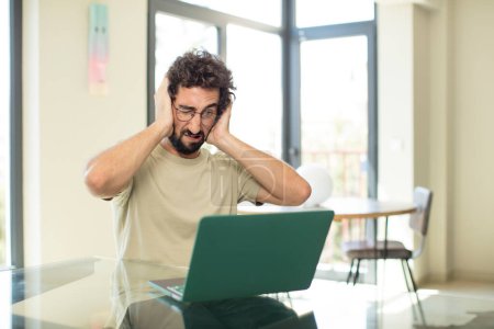 Téléchargez les photos : Jeune homme barbu adulte avec un ordinateur portable se sentant frustré et agacé, malade et fatigué de l'échec, fatigué des tâches ennuyeuses et ennuyeuses - en image libre de droit