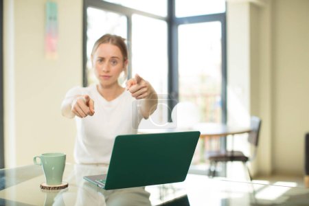 Photo for Caucasian pretty woman with a laptop pointing forward at camera with both fingers and angry expression, telling you to do your duty - Royalty Free Image