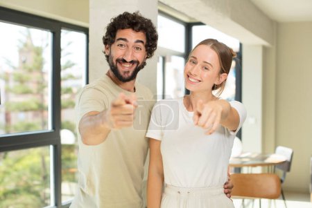 Téléchargez les photos : Jeune couple adulte pointant vers la caméra avec un sourire satisfait, confiant et amical, vous choisissant - en image libre de droit