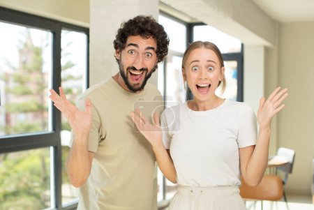 Photo for Young adult couple feeling happy, excited, surprised or shocked, smiling and astonished at something unbelievable - Royalty Free Image