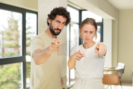Photo for Young adult couple pointing forward at camera with both fingers and angry expression, telling you to do your duty - Royalty Free Image