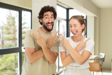 Photo for Young adult couple smiling and looking happy, friendly and satisfied, gesturing victory or peace with both hands - Royalty Free Image